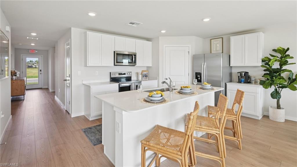 5007 3rd Street West Lehigh Acres, FL 33971 - Photo 9 of 24 Model Home. The kitchen features a large island with a sink, white cabinetry, and stainless steel appliances, including an oven, microwave, and refrigerator