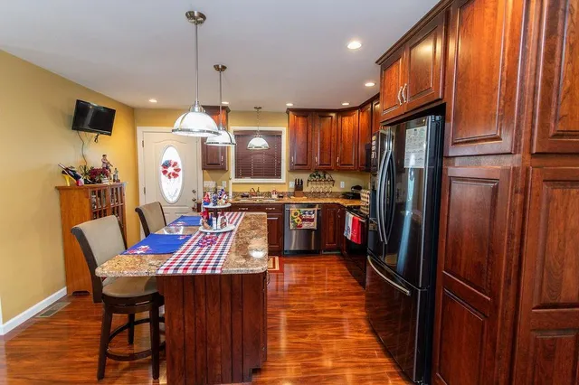 a kitchen with stainless steel appliances granite countertop a refrigerator a sink dishwasher and wooden cabinets with wooden floor