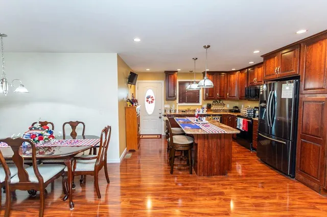 a kitchen with stainless steel appliances granite countertop a dining table chairs refrigerator and sink