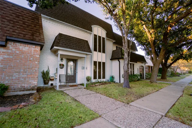 a view of a house with a small yard plants and a large tree