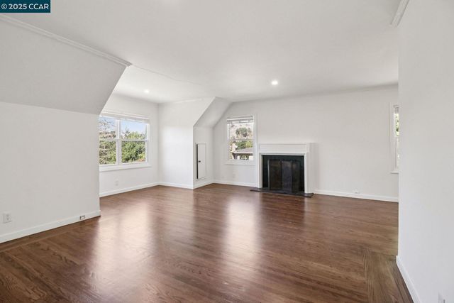 an empty room with wooden floor fireplace and windows