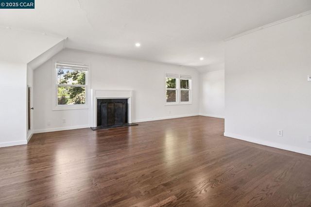 an empty room with wooden floor fireplace and windows