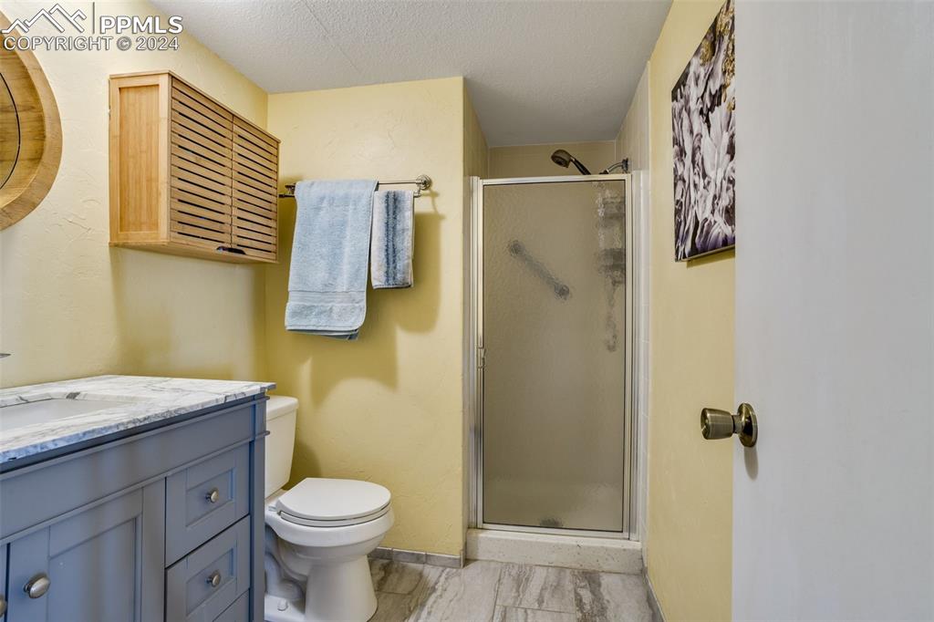 1098 Fontmore Road, Unit B Colorado Springs, CO 80904 - Photo 17 of 27 Bathroom featuring toilet, a shower with door, vanity, and a textured ceiling