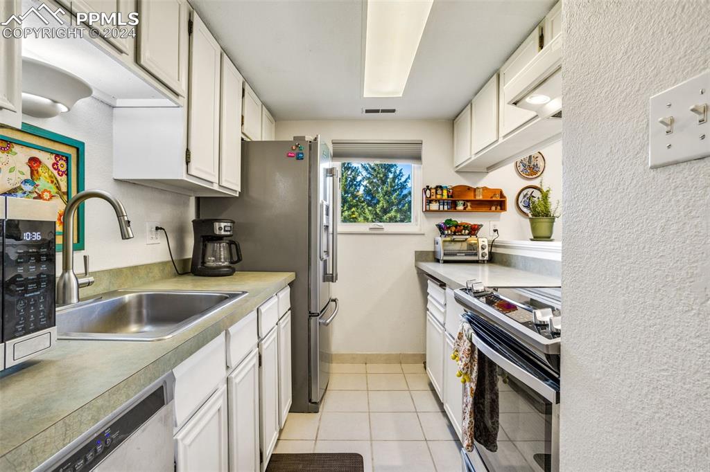 1098 Fontmore Road, Unit B Colorado Springs, CO 80904 - Photo 8 of 27 Kitchen with stove, light tile patterned floors, sink, stainless steel dishwasher, and white cabinetry