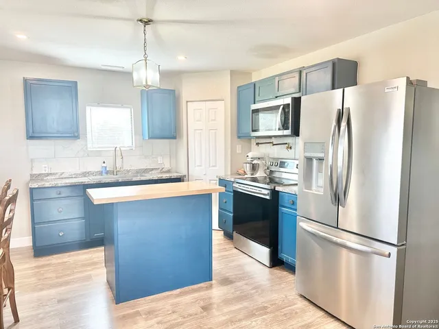 a kitchen with kitchen island granite countertop a refrigerator a sink dishwasher a stove and white cabinets with wooden floor