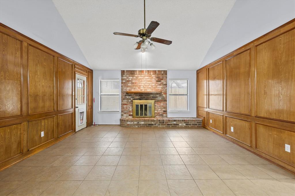 Unfurnished living room with a ceiling fan, a brick fireplace, light tile patterned flooring, and vaulted ceiling