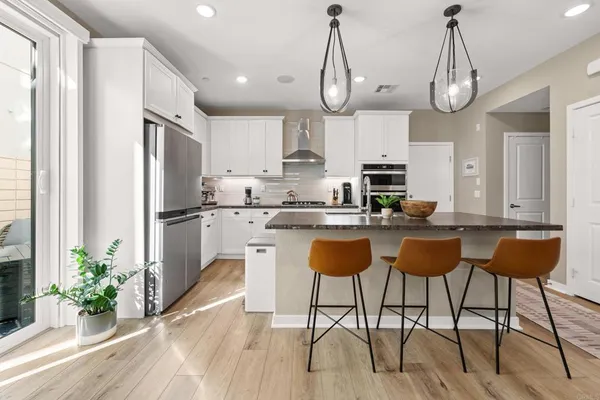 a kitchen with stainless steel appliances granite countertop a refrigerator a sink dishwasher a dining table and chairs with wooden floor