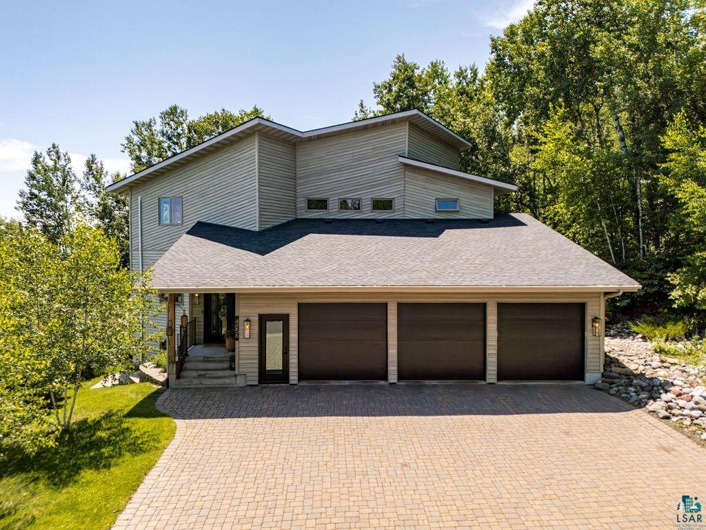 4856 Kingston Street Duluth, MN 55804 - Photo 1 of 88 Contemporary multi-level residence featuring light-toned horizontal siding, a dark shingled roof, a three-car garage with dark doors, a paver driveway, and an entryway with a dark door and side panel