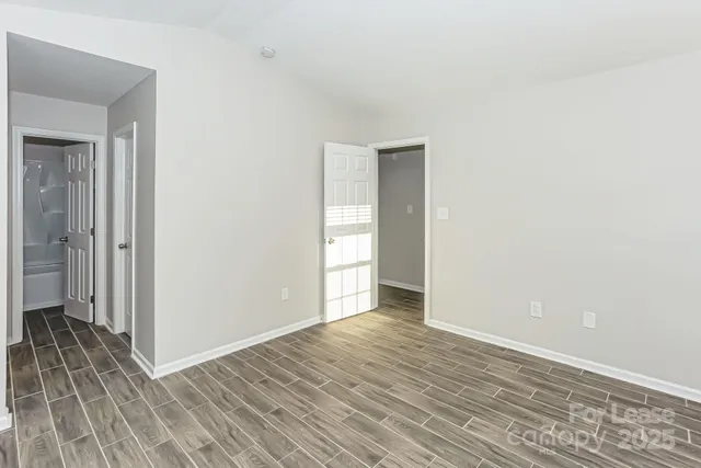 a view of an empty room with wooden floor and a bedroom