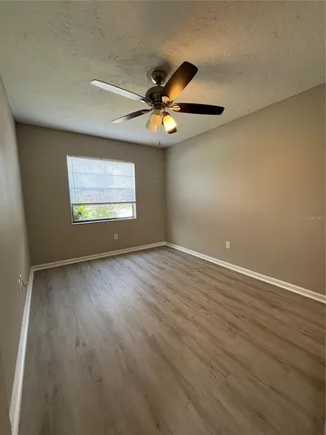 an empty room with wooden floor chandelier fan and windows