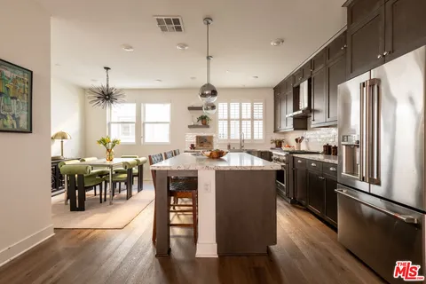 a kitchen with stainless steel appliances granite countertop a refrigerator a stove top oven a sink dishwasher a dining table and chairs with wooden floor