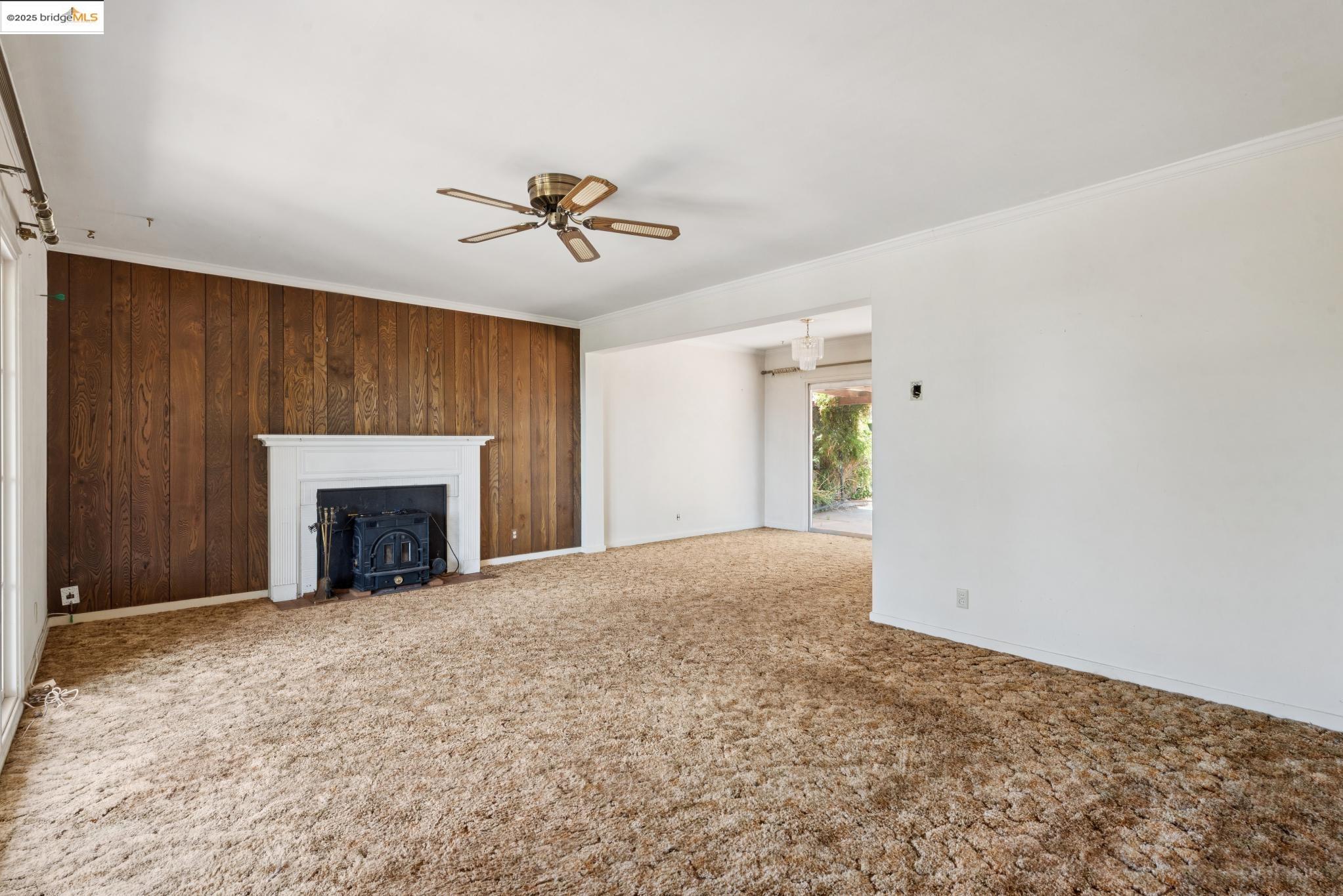4751 Lincoln Avenue Oakland, CA 94602 - Photo 11 of 60 Unfurnished living room featuring ornamental molding, wood walls, carpet flooring, ceiling fan, and a wood stove