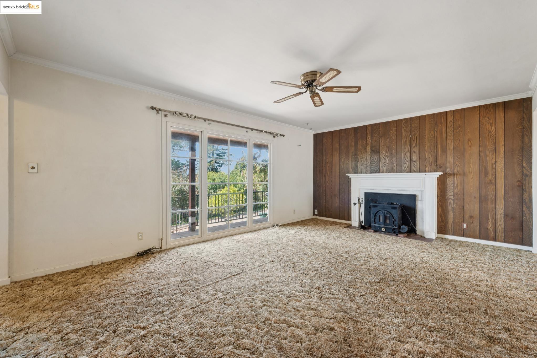 4751 Lincoln Avenue Oakland, CA 94602 - Photo 9 of 60 Unfurnished living room with ornamental molding, carpet floors, ceiling fan, a wood stove, and wood walls