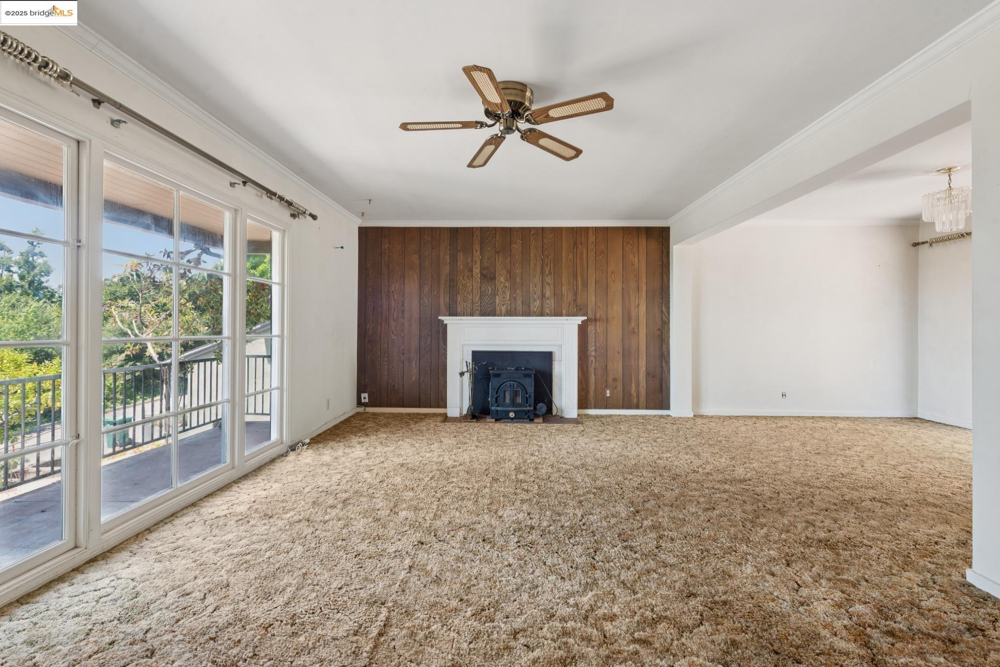 4751 Lincoln Avenue Oakland, CA 94602 - Photo 10 of 60 Unfurnished living room with crown molding, a wood stove, carpet floors, a ceiling fan, and wood walls