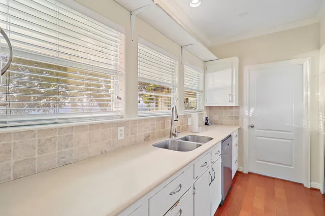 a kitchen with stainless steel appliances granite countertop a stove a sink and white cabinets with wooden floor next to windows