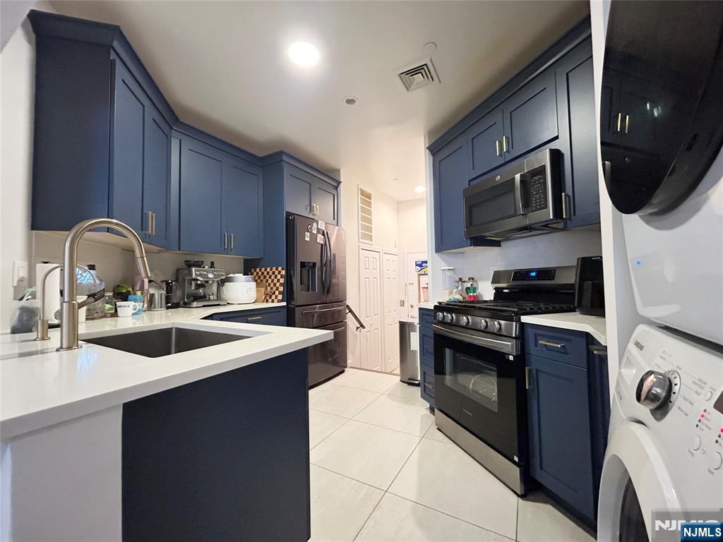 18 Independence Way, Unit J018 Edgewater, NJ 07020 - Photo 12 of 18 a kitchen with stainless steel appliances granite countertop a sink a stove top oven a refrigerator with wooden cabinets and floor