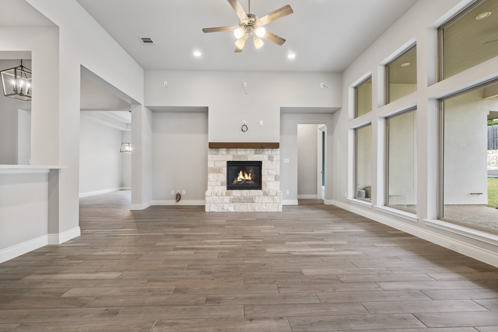104 Catani Loop Georgetown, TX 78628 - Photo 3 of 34 Spacious living area featuring wood-look tile flooring, a stone fireplace with a wood mantle, and a ceiling fan with light fixture