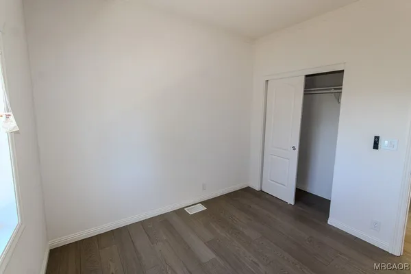a view of an empty room with wooden floor and closet