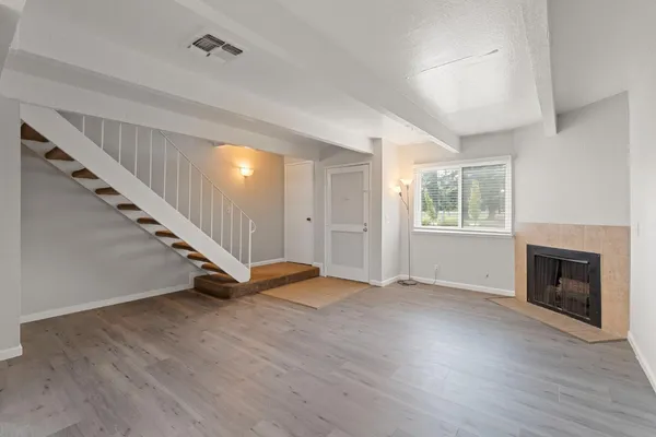 a view of an empty room with wooden floor a fireplace and a window