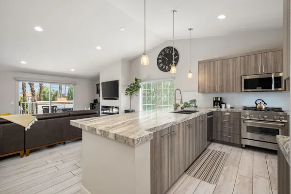 a kitchen with stainless steel appliances granite countertop a stove top oven a sink dishwasher a refrigerator and a dining table with wooden floor
