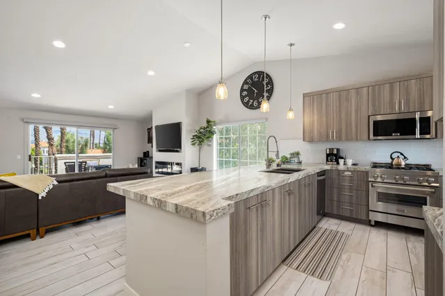 a kitchen with stainless steel appliances granite countertop a stove top oven a sink dishwasher a refrigerator and a dining table with wooden floor