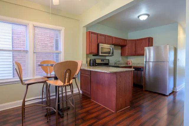 a kitchen with stainless steel appliances granite countertop a refrigerator a stove top oven a sink dishwasher and a dining table with wooden floor