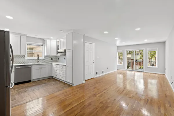 a large white kitchen with granite countertop a stove top oven a sink dishwasher and a refrigerator with wooden floor