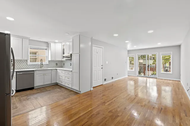 a large white kitchen with granite countertop a stove top oven a sink dishwasher and a refrigerator with wooden floor