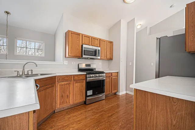 a kitchen with stainless steel appliances a stove a sink a refrigerator white cabinets and wooden floor