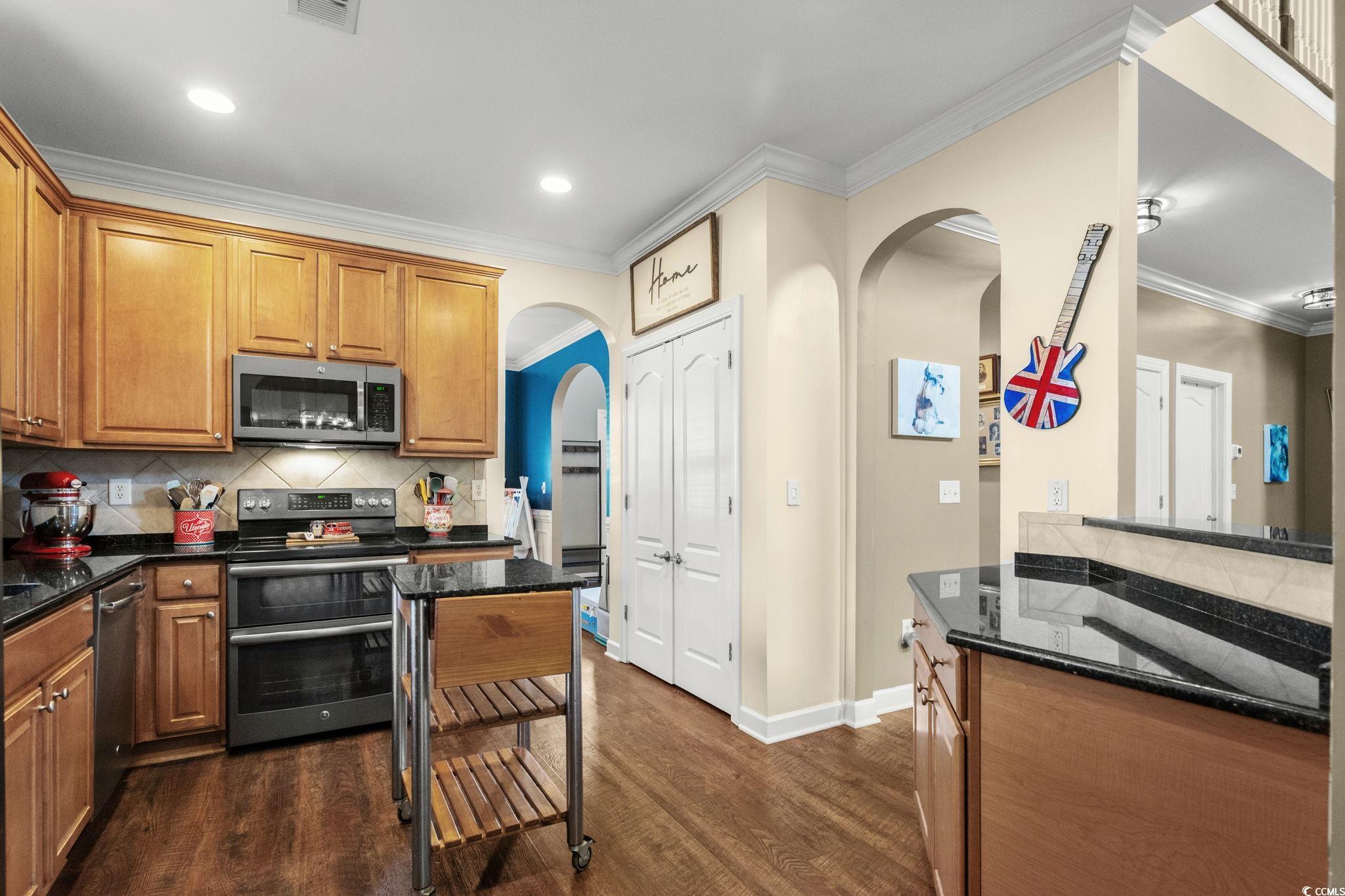 318 Barlow Court Conway, SC 29526 - Photo 11 of 36 Kitchen featuring dark stone counters, stainless steel appliances, arched walkways, ornamental molding, and brown cabinetry