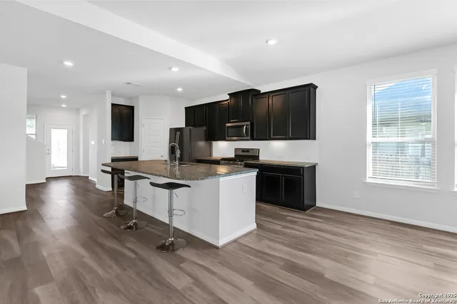 a kitchen with stainless steel appliances granite countertop a stove top oven a sink dishwasher a refrigerator and a dining table with wooden floor