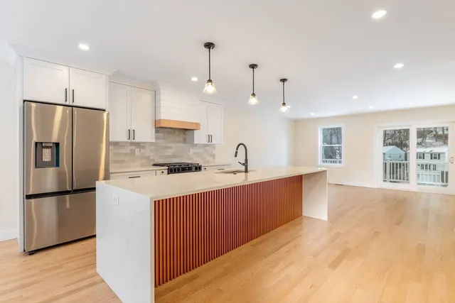 a large kitchen with stainless steel appliances granite countertop a refrigerator a sink dishwasher a stove and a refrigerator with wooden floor