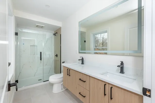a spacious bathroom with a double vanity sink toilet mirror and shower