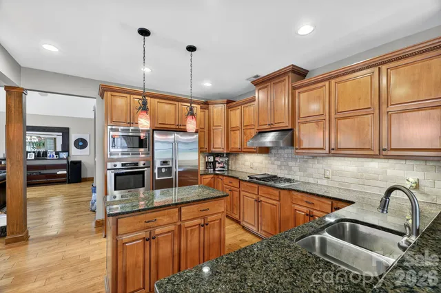 a kitchen with stainless steel appliances granite countertop a sink a stove and a wooden floors