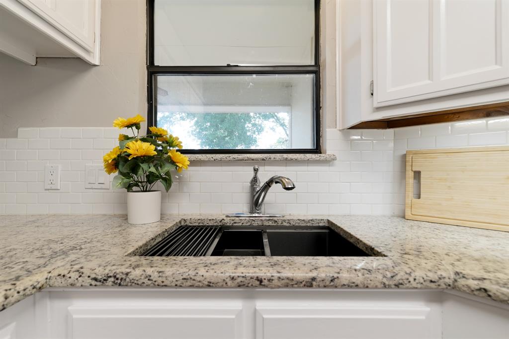 6612 Patsy Lane Watauga, TX 76148 - Photo 16 of 32 Kitchen sink featuring a dual-basin workstation sink with integrated drying rack, a gooseneck faucet, light-toned granite countertops, white subway tile backsplash, and white cabinetry