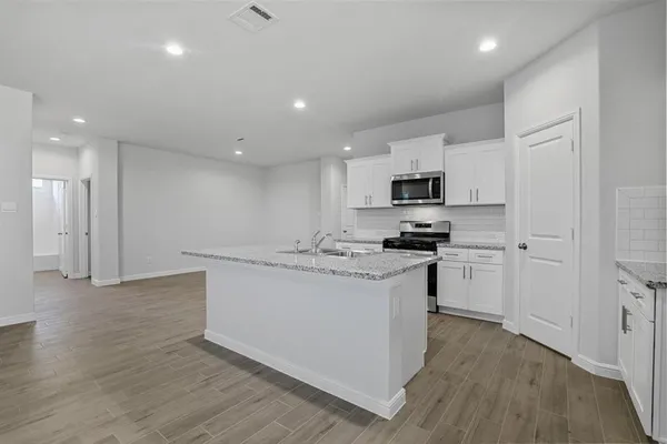 a kitchen with stainless steel appliances granite countertop a stove top oven a sink a refrigerator and white cabinets with wooden floor