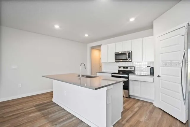 a kitchen with stainless steel appliances granite countertop a sink dishwasher a stove and a refrigerator with wooden floor