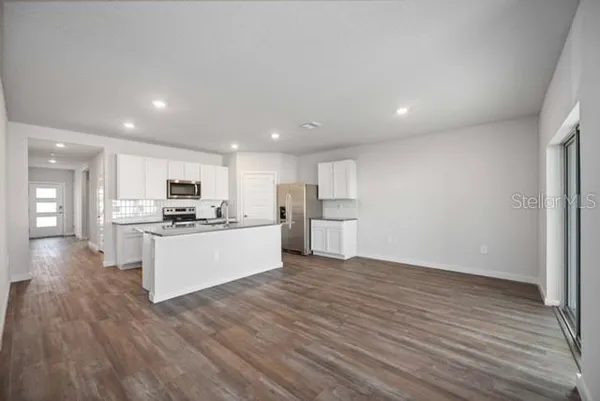 a view of kitchen with kitchen island granite countertop a stove top oven a sink and white cabinets with wooden floor