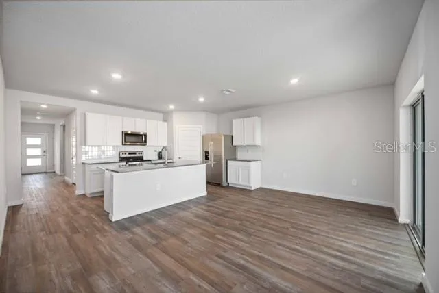 a view of kitchen with kitchen island granite countertop a stove top oven a sink and white cabinets with wooden floor