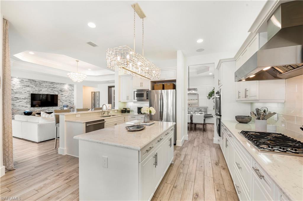 4353 Caldera Circle Naples, FL 34119 - Photo 5 of 40 a large white kitchen with a stove a sink dishwasher and a dining table with wooden floor