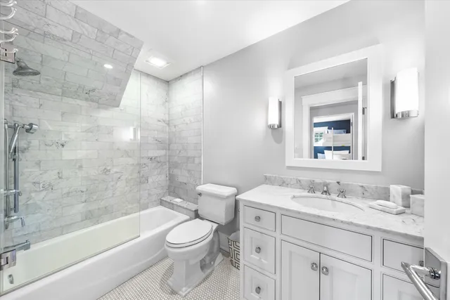 a bathroom with a granite countertop toilet a sink a mirror a bathtub and shower