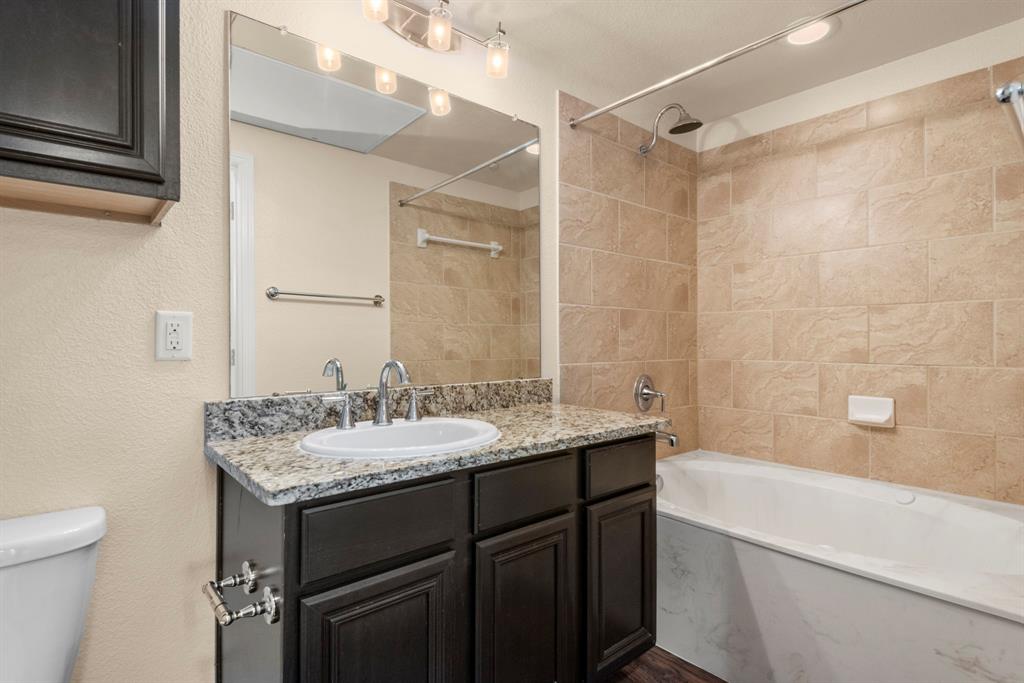 a bathroom with a granite countertop sink a toilet a mirror and shower