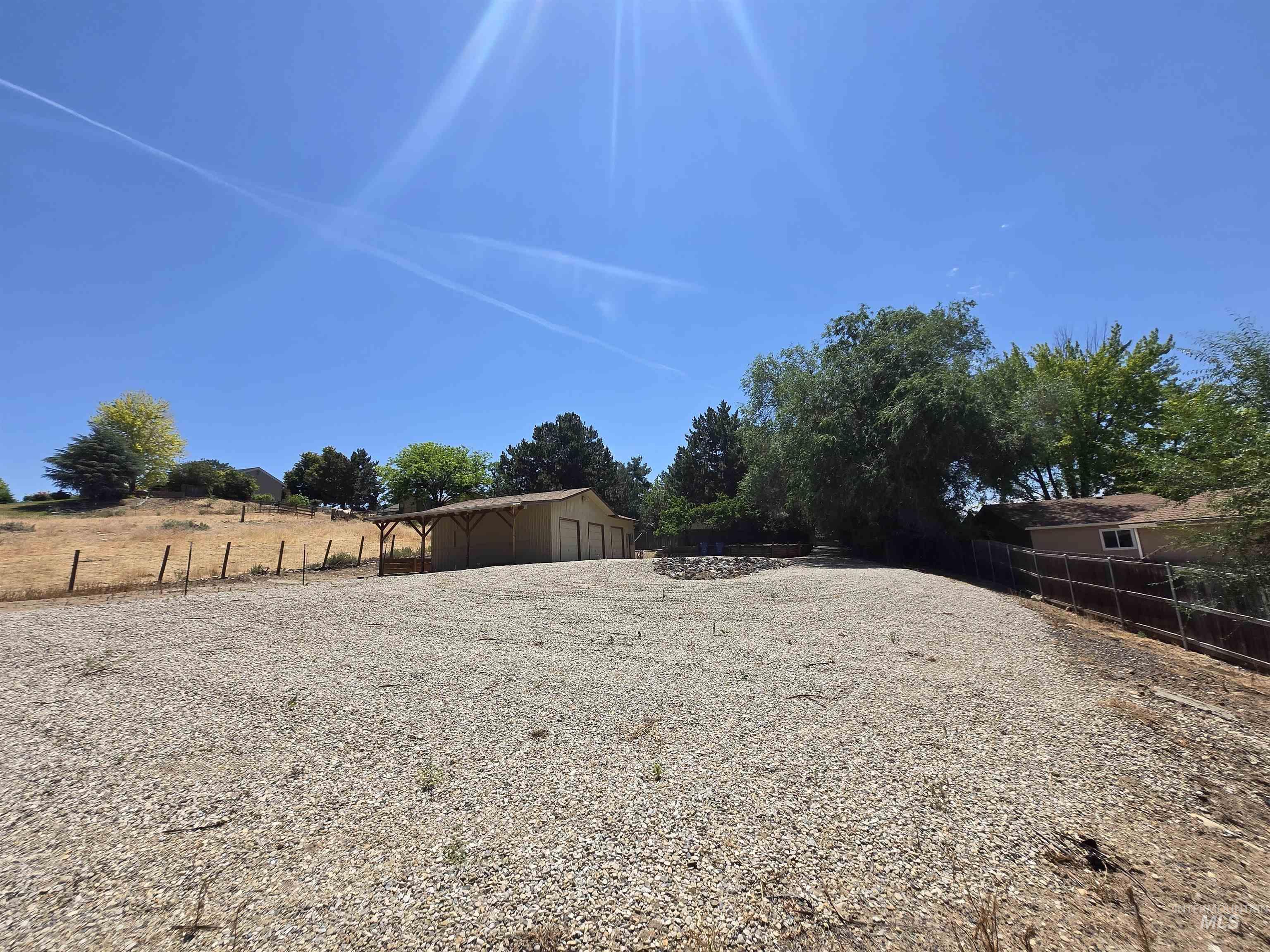 12050 West Hidden Valley Rim Road Boise, ID 83709 - Photo 35 of 39 Expansive gravel-covered lot featuring a three-bay garage structure with an attached covered patio