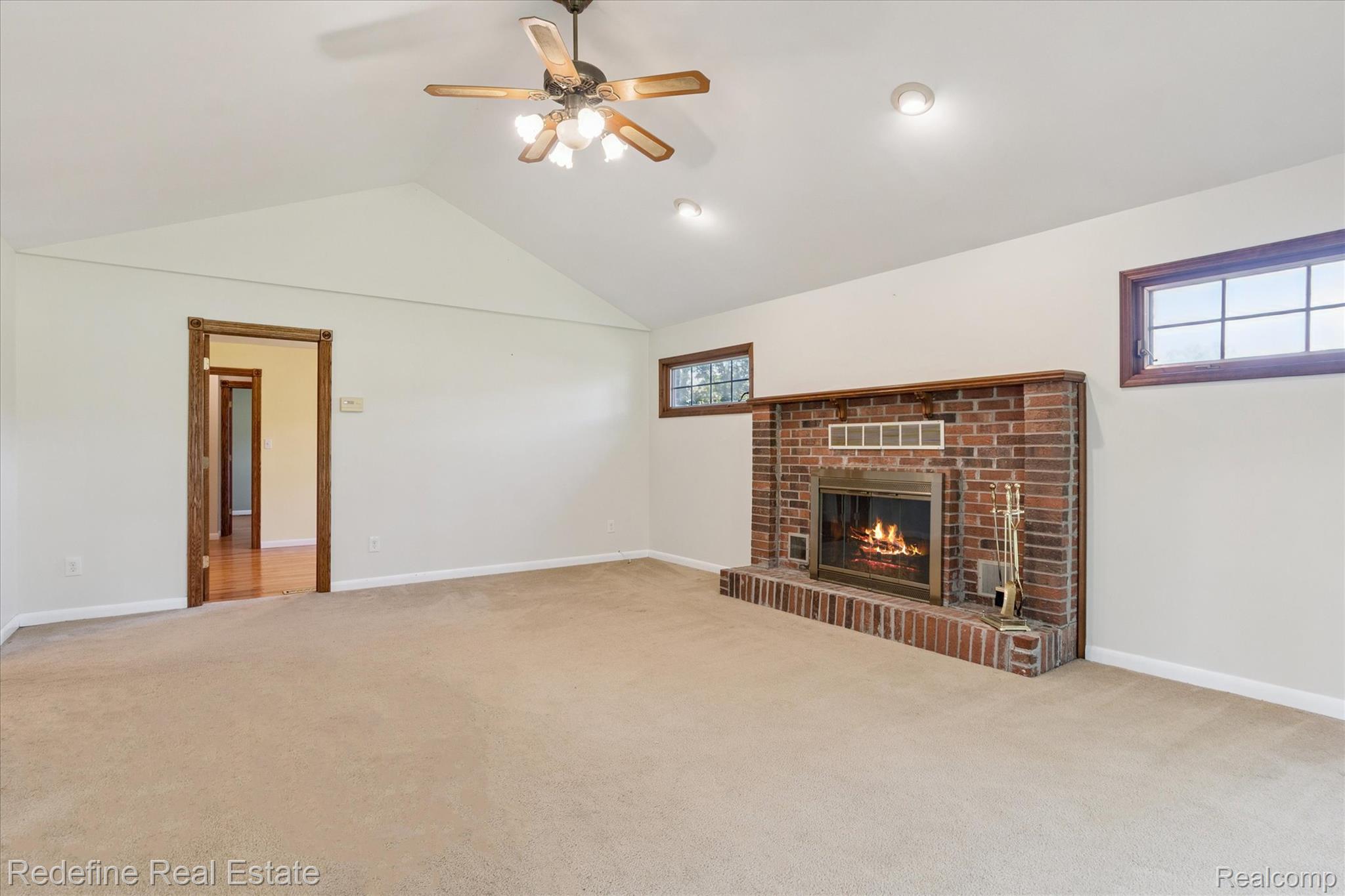 3777 Dorr Road Brighton, MI 48116 - Photo 28 of 77 Unfurnished living room featuring vaulted ceiling, a brick fireplace, light colored carpet, and a ceiling fan