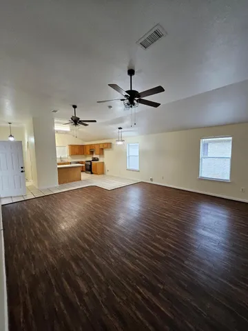 an empty room with wooden floor a ceiling fan and windows