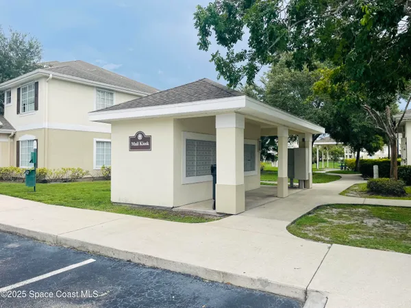 a view of a white house with a small yard plants and a large tree