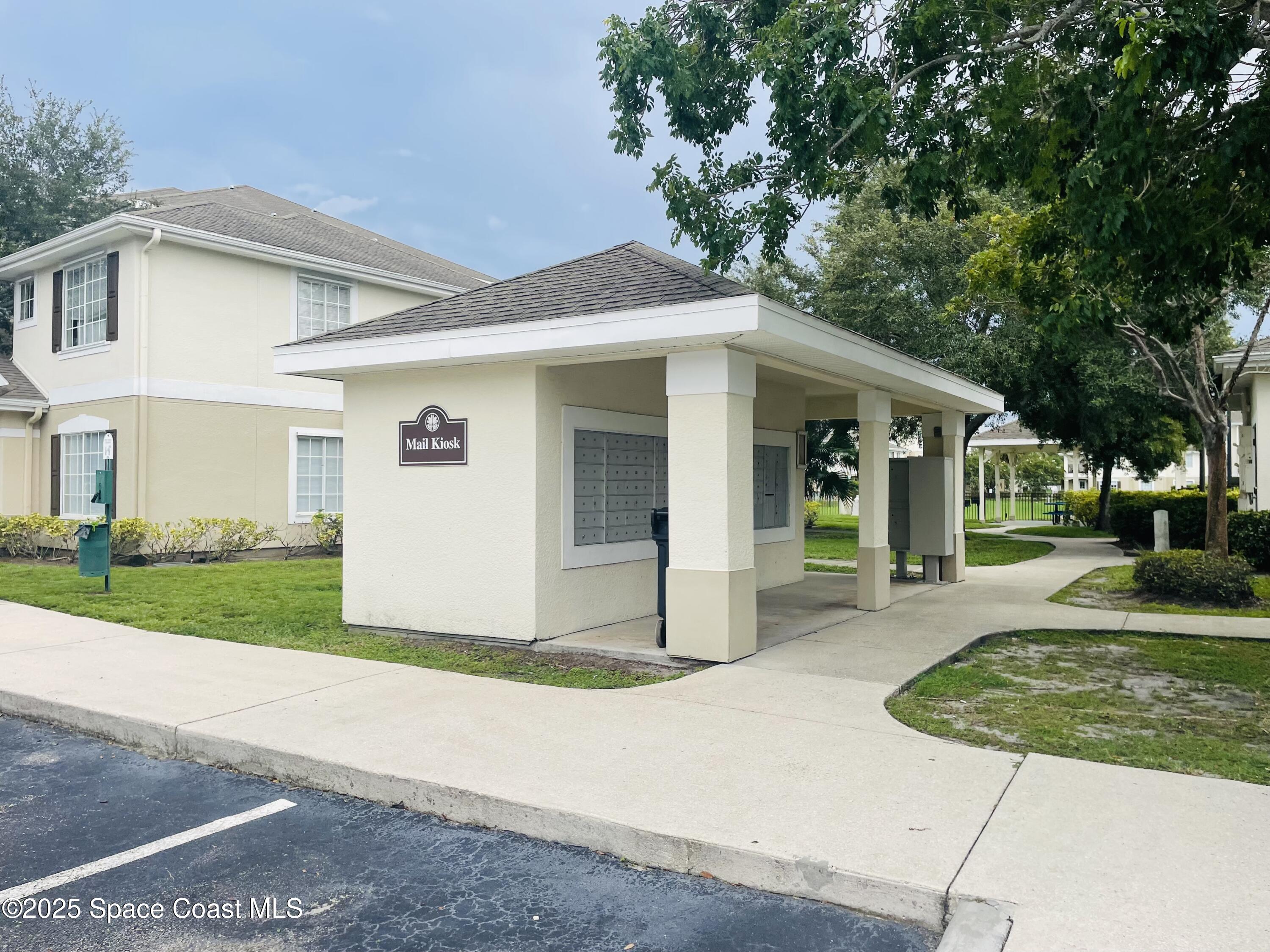 3501 D D'Avinci Way, Unit 1011 Melbourne, FL 32901 - Photo 16 of 19 a view of a white house with a small yard plants and a large tree