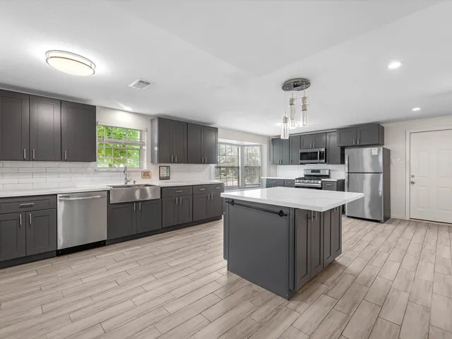a large kitchen with stainless steel appliances kitchen island granite countertop wooden floors and a view of living room