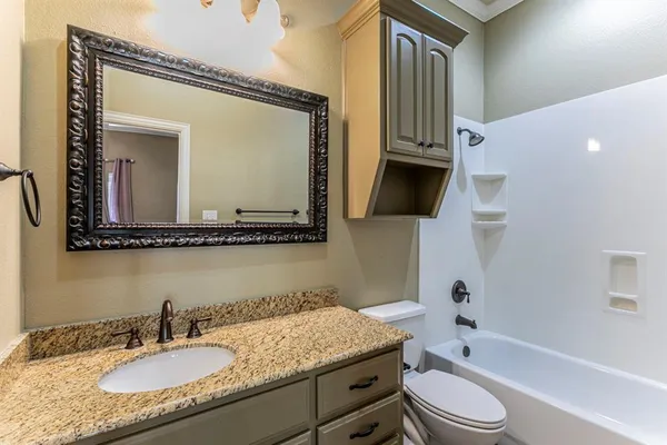a bathroom with a granite countertop sink vanity mirror bathtub shower and a toilet