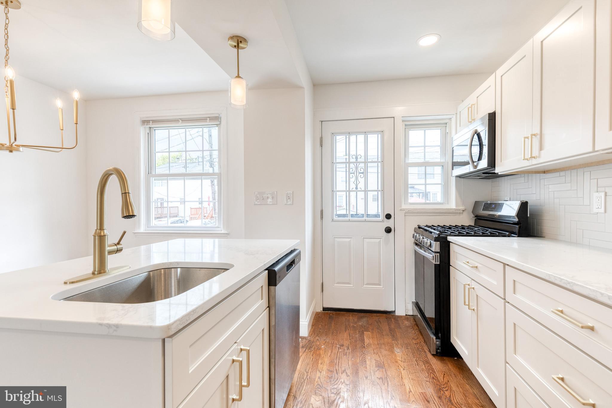 2708 Uhler Avenue Baltimore, MD 21215 - Photo 6 of 18 a kitchen with white cabinets a sink dishwasher and a stove with wooden floor
